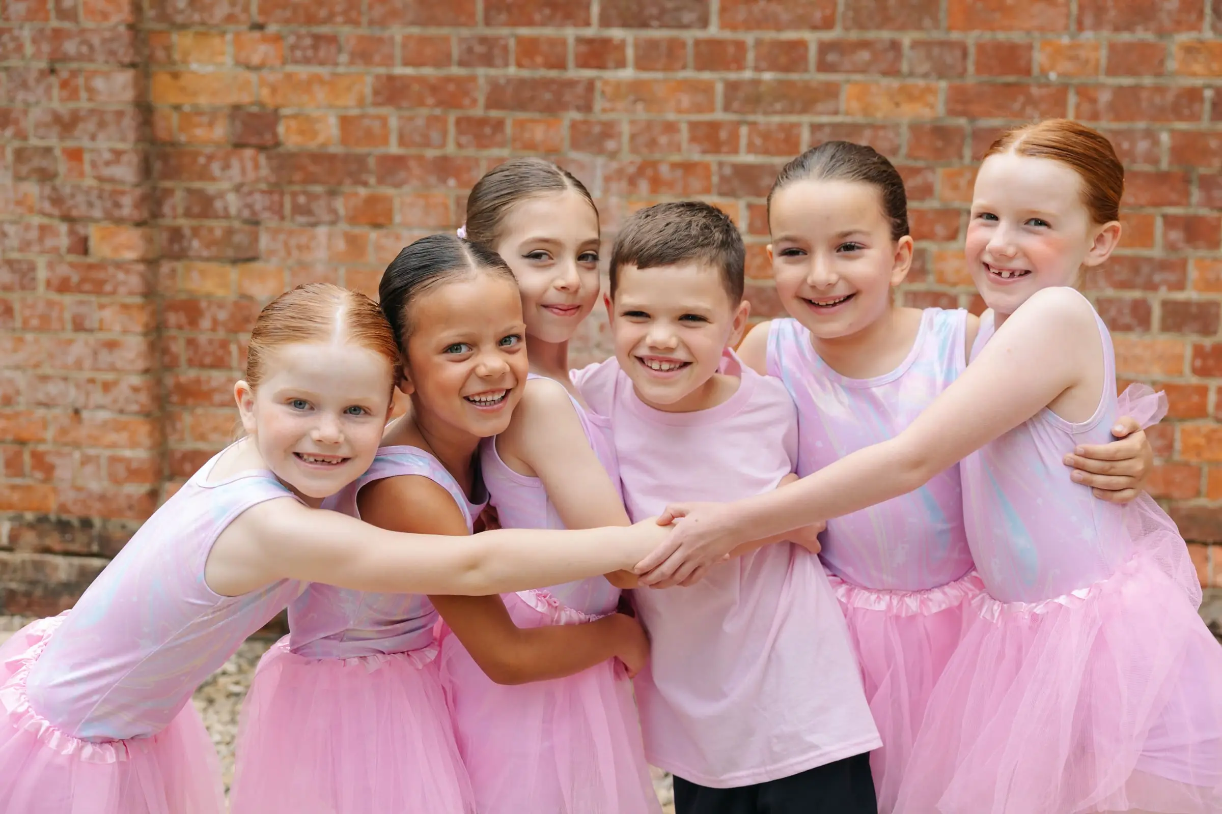 A group of smiling young Dancemania dancers in pink tutus, arms linked together