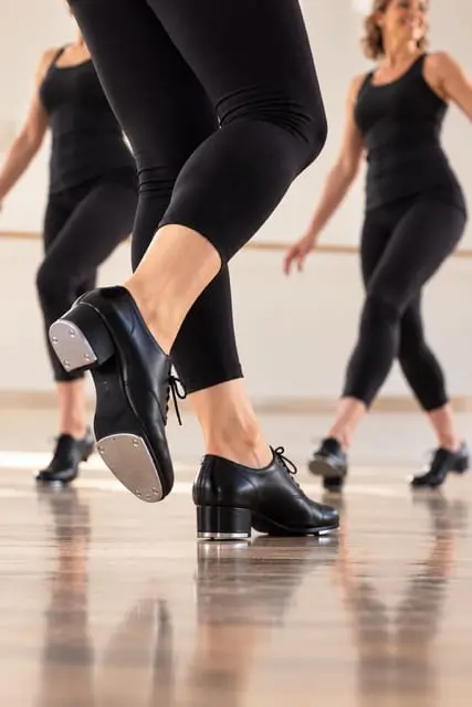 Adult dancers in tap shoes mid-step in a beginner tap class