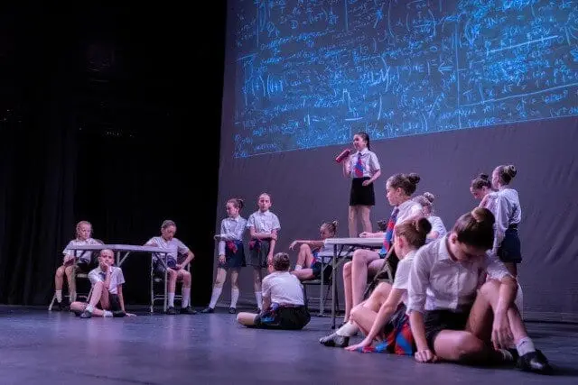 Dancemania students in school uniform performing a musical theatre scene on stage