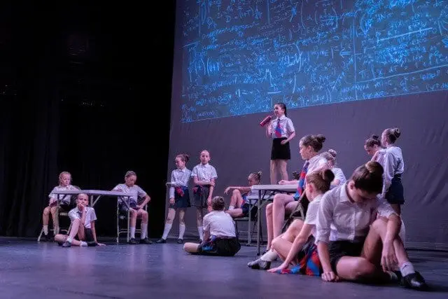 Dancemania students in school uniform performing a musical theatre scene on stage